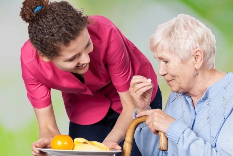 Betreuerin reicht Teller mit Obst an Klientin: Unterstützung bei der Lebensführung